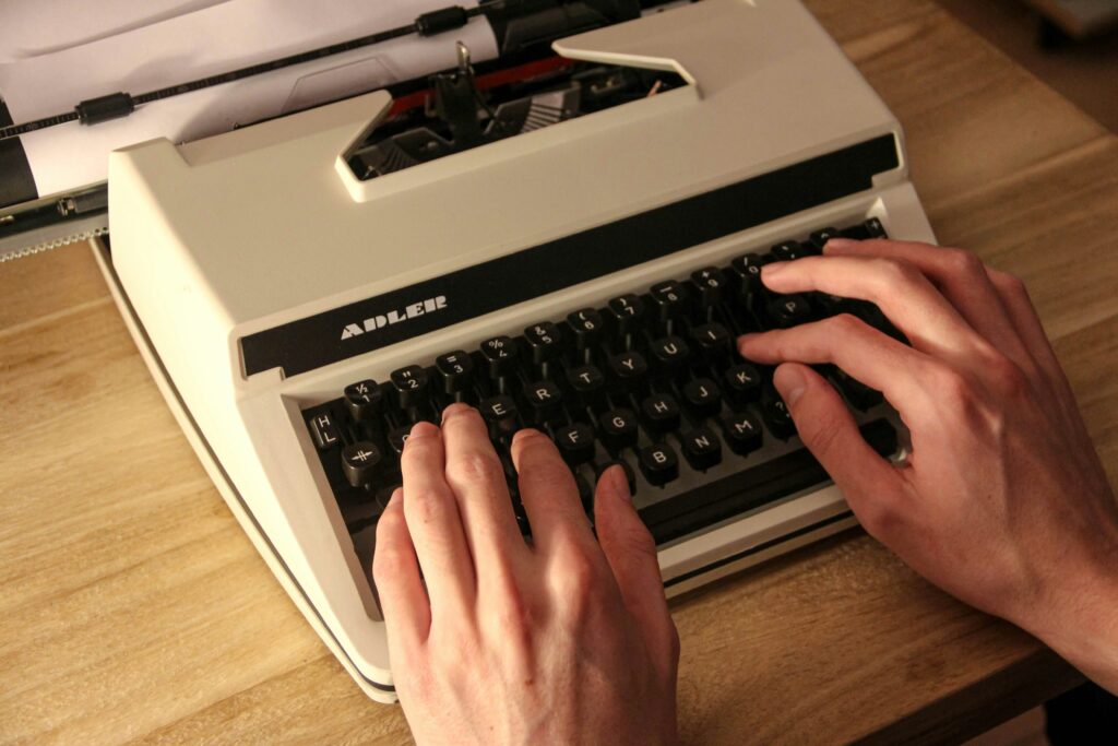 Hands typing on a white Adler typewriter placed on a wooden desk, evoking a sense of nostalgia and retro charm.